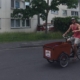 Mann mit rotem Tanktop und Cappie fährt auf Lastenrad über eine Straße